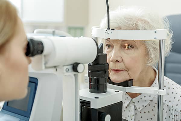 Optometrist using a tonometer on an old woman during an eye test.