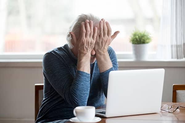 Old man rubbing his eyes with both hands in front of a laptop because of dry eye disease