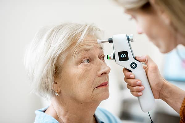 An optometrist uses a tonometer on a woman during a corneal treatment consultation
